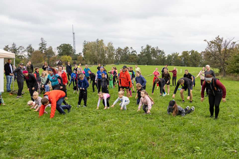 Děti a dospělí se společně rozcvičují na louce před během.